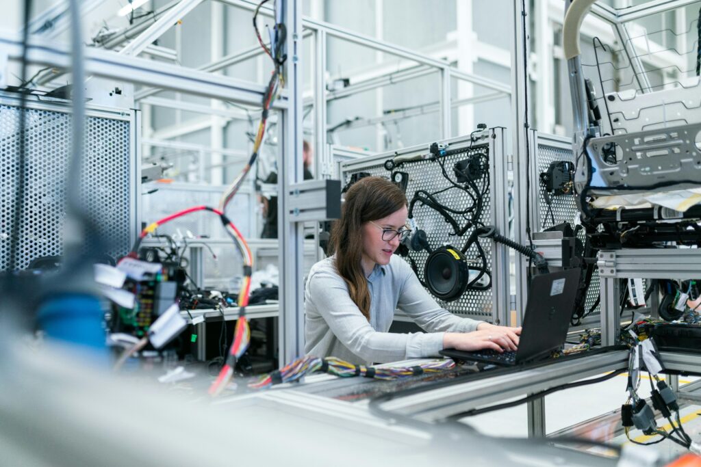 A female engineer focuses on her laptop amidst advanced tech equipment in a lab.